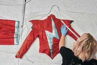A person wearing blue gloves uses a tape measure to measure a red jacket with a blue and white lightning flash on the back